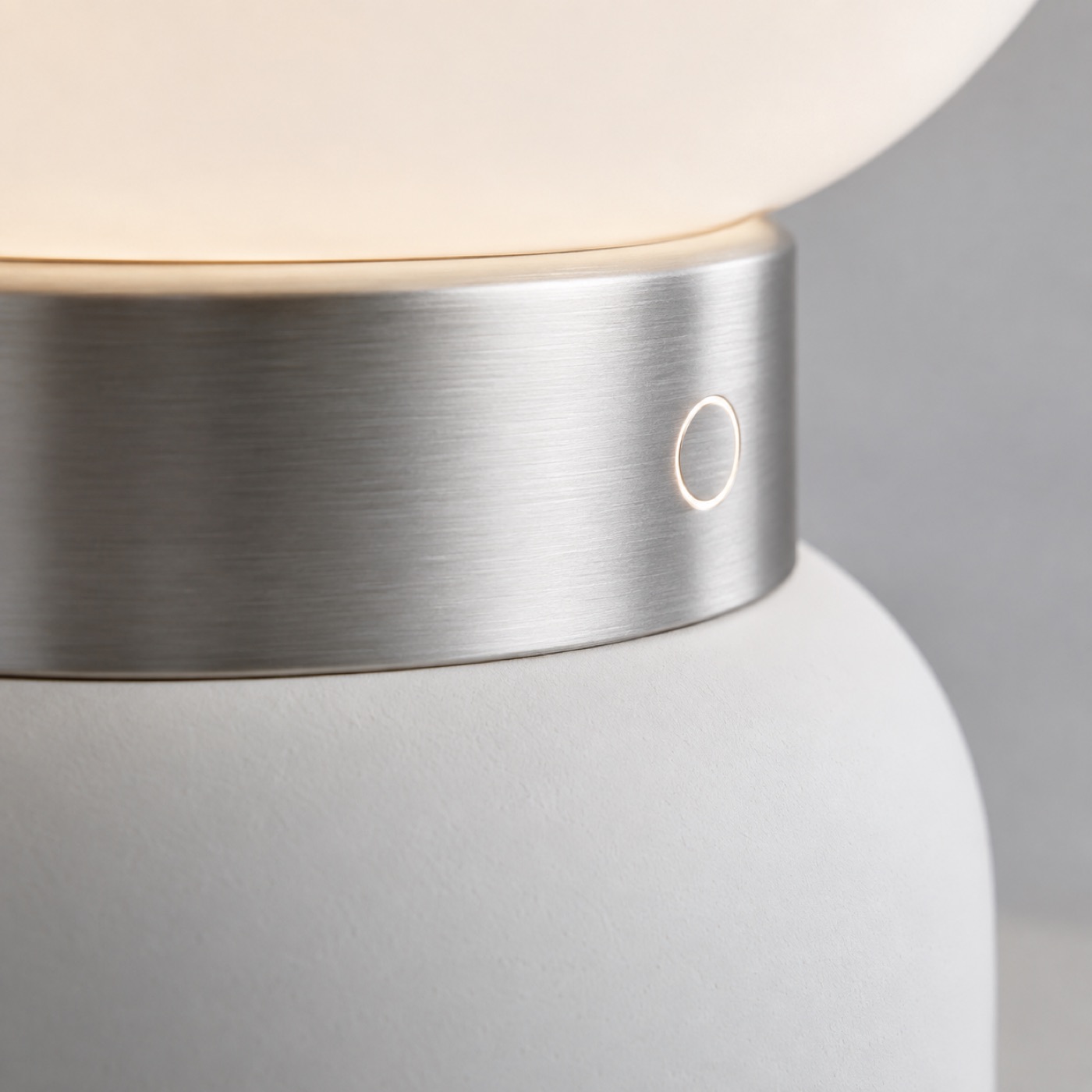 Närbild där borstat aluminium möter matt keramik, med en upplyst pekring